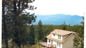 A two-story house with a balcony, surrounded by dense forest and mountains in the background. - Rocky Mountain Getaway (Plains)