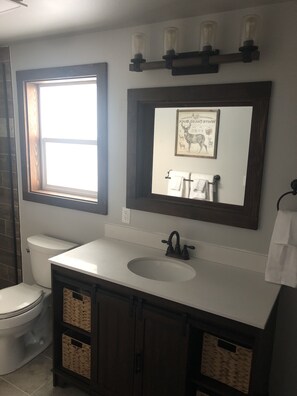 A bathroom with a white sink, dark wooden cabinets, a mirror, and a window. - Rocky Mountain Getaway (Plains)
