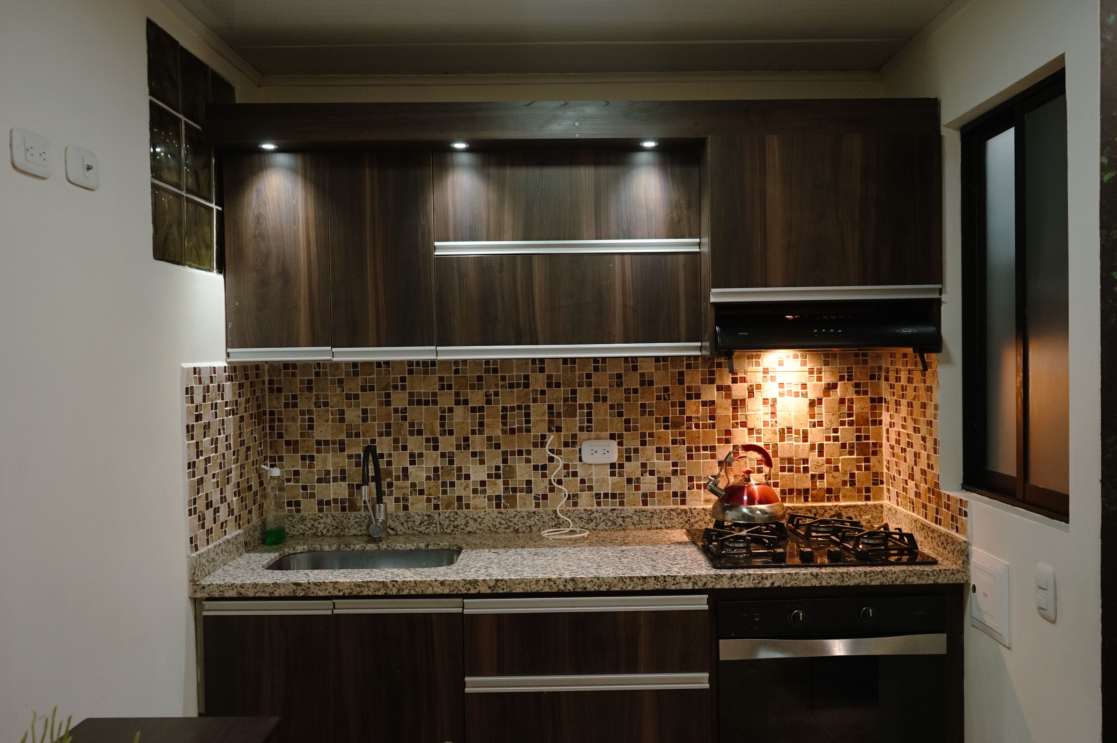 Una cocina moderna con alacenas de madera oscura, salpicadero de azulejos, estufa a gas y electrodomésticos de acero inoxidable.