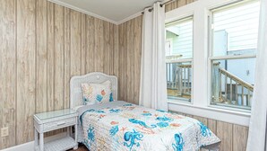 A bedroom with a bed, a glass bedside table, a wooden wall, and a window with a view of a balcony.