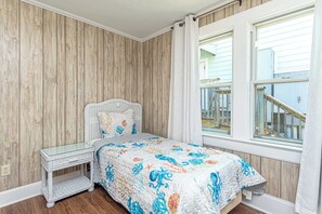 A bedroom with a bed, a glass bedside table, a wooden wall, and a window with a view of a balcony.