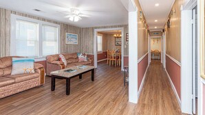 A spacious living room with a wooden floor, a ceiling fan, and a dining area with a table and chairs.