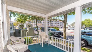 A covered porch with wicker furniture, a view of the street, and a building in the background.