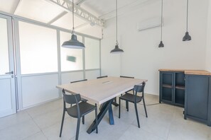 Sala de conferências com uma mesa grande, quatro cadeiras e três luminárias pendentes.