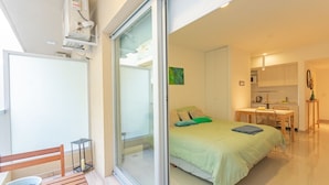 A modern bedroom with a sliding glass door leading to a balcony, a small kitchenette, and a dining area. - Paseo de las Cisternas (Buenos Aires)