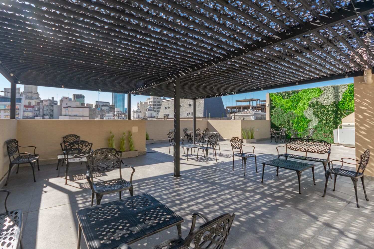 An outdoor patio with metal furniture, a pergola, and a green wall.