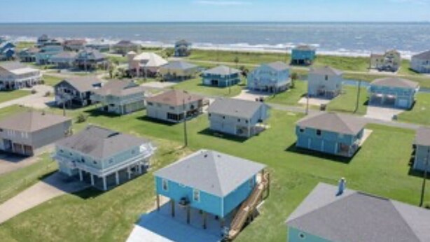 A coastal residential area with houses arranged in rows, a clear view of the ocean, and a grassy landscape. - Beach Blessing with ocean view, 3br/2bath sleeps 8 (Bolivar Peninsula)