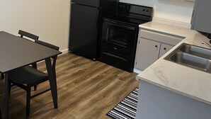 Angolo cottura attrezzato con frigorifero, fornello, forno e lavello. Un tavolo con sedie e un tappeto decorativo.