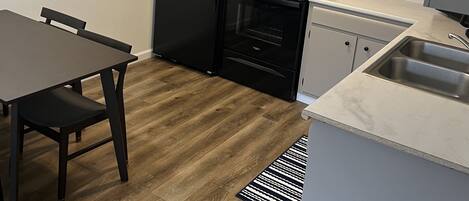 Une cuisine compacte équipée d’un réfrigérateur, d’une cuisinière, d’un four et d’un évier. On y trouve une table à manger avec des chaises et un tapis à motifs.