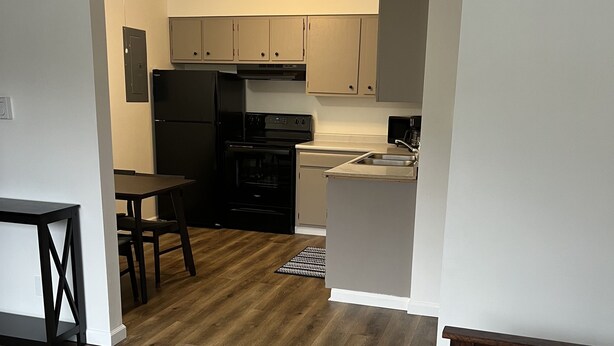 Una cucina moderna con frigorifero, piano cottura e forno neri, un'area pranzo con tavolo e sedie e un divano grigio nella zona soggiorno.