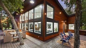 Une cabane moderne en bois, dotée de grandes fenêtres, d’un espace salon extérieur et de guirlandes lumineuses.