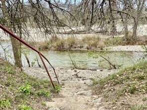 Un cadre naturel en plein air, avec une étendue d’eau claire, un sentier de pierres et une végétation clairsemée.