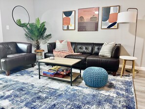 A living room with a black leather sofa, a coffee table, a blue knitted pouf, and a blue and white patterned rug. - Beautifully remodeled 2 bedroom, 2 bath condo in a great location (Phoenix)