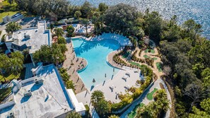 An aerial view of a resort with a large, curved swimming pool surrounded by lounge areas and a golf course. - Retreat 5 Bed Townhouse screened Private Pool*Amazing price (Davenport)