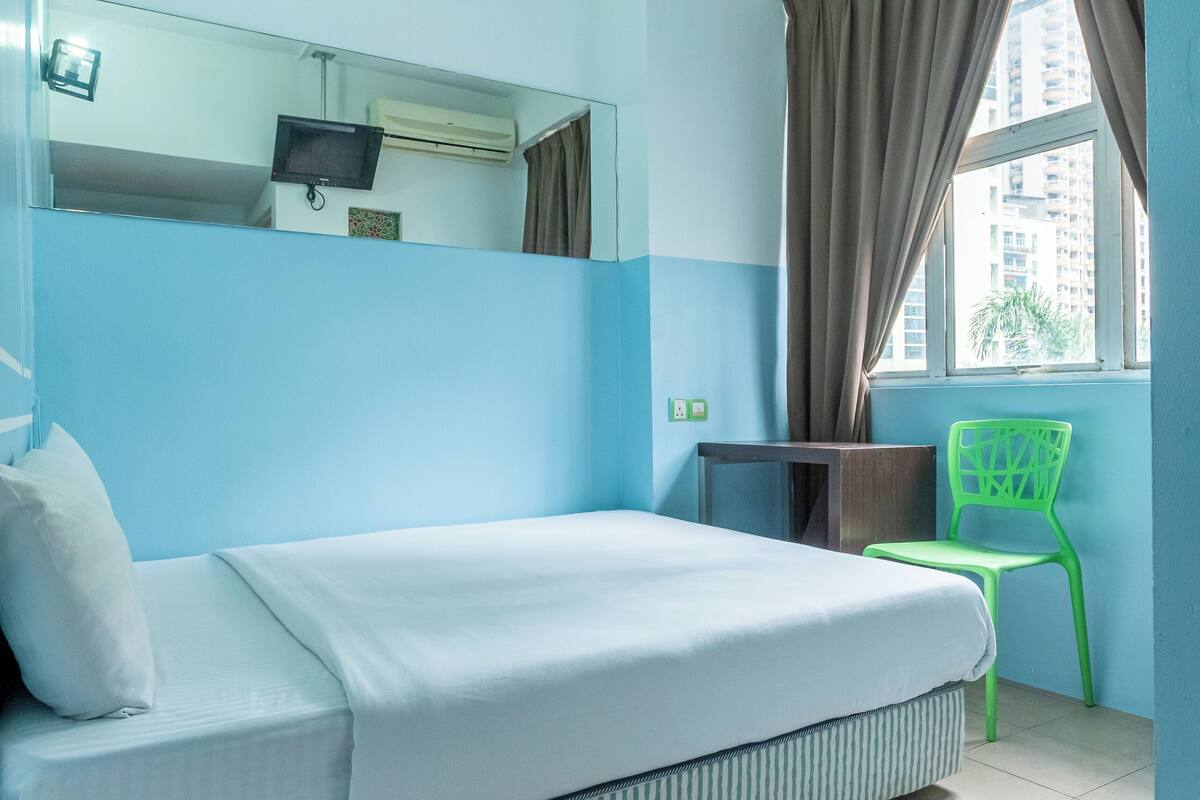 Een hotelkamer met een bed, een stoel, een televisie en een raam met gordijnen.