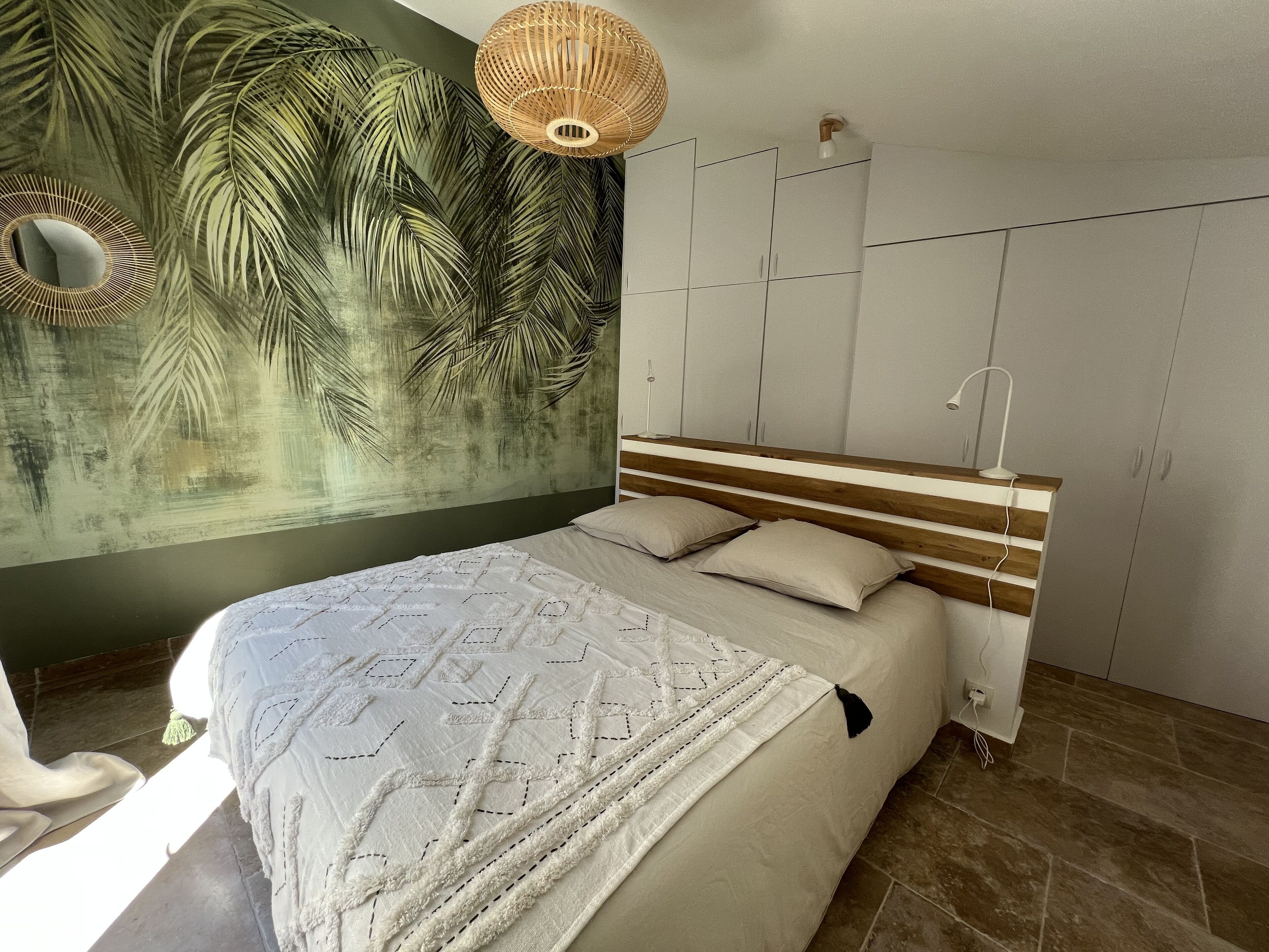 A bedroom with a bed, a wall mural, a wardrobe, and a hanging light fixture.