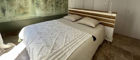 A bedroom with a bed, a wall mural, a wardrobe, and a hanging light fixture.