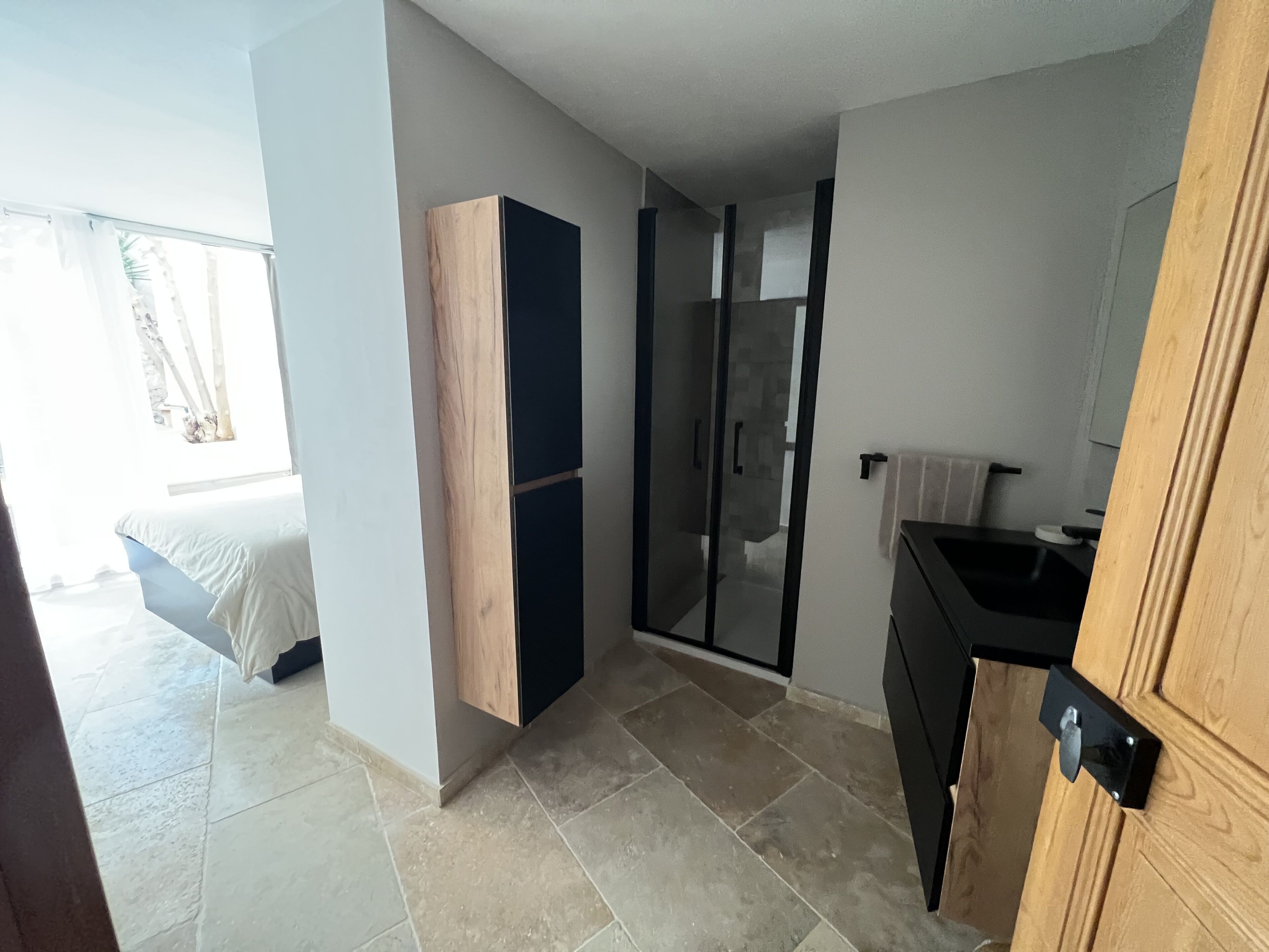 A modern kitchen with a wooden cabinet, a black countertop, and a glass shower enclosure.