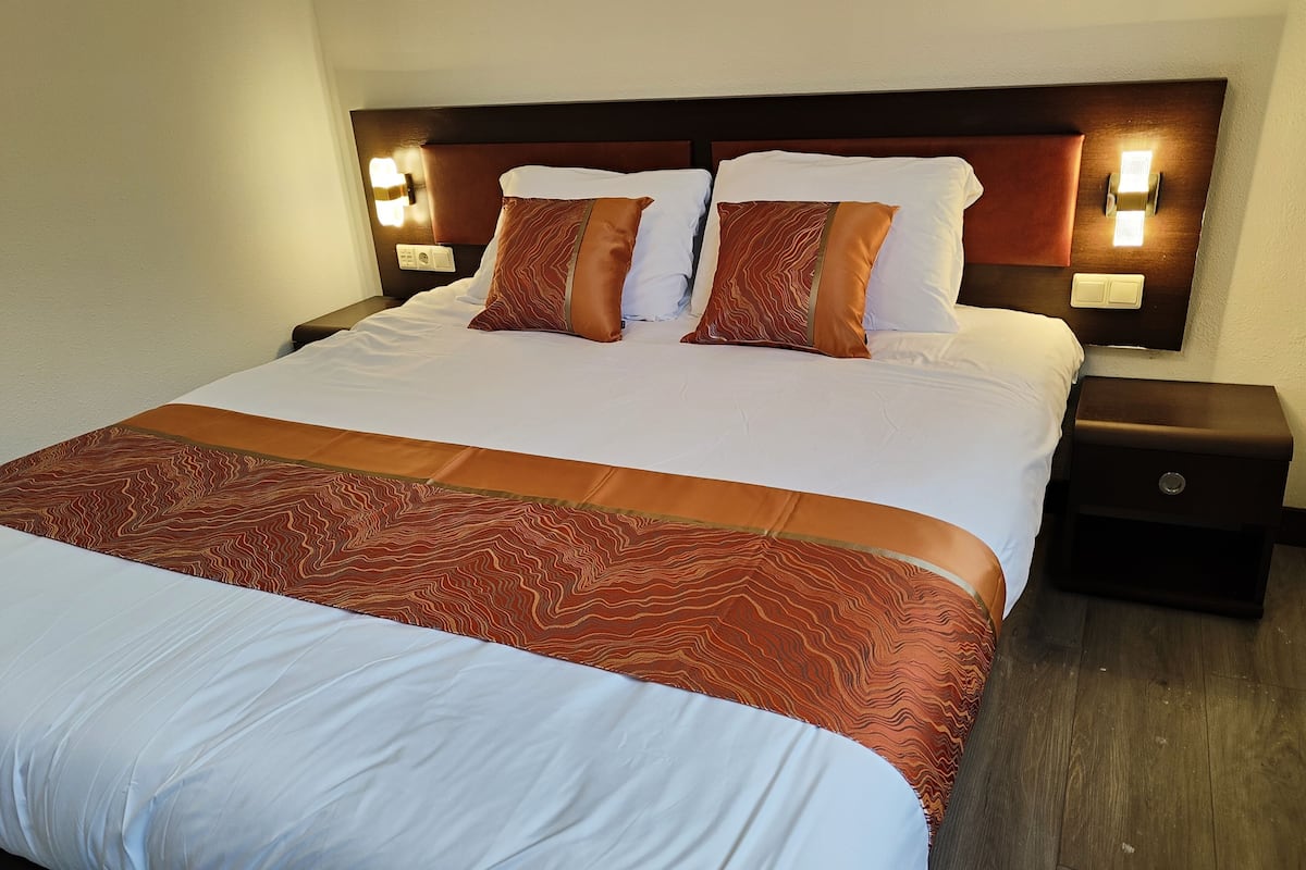 Une chambre d’hôtel avec un grand lit, deux tables de chevet et une tête de lit en bois.