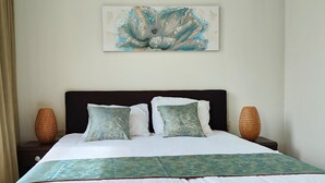 Una cama bien hecha con una colcha blanca y verde, dos almohadas a juego y un adorno decorativo en la pared.