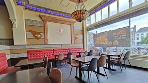 Interior de un restaurante con asientos tipo banca rojos, mesas y sillas de madera. Se ve un ventanal con vistas a la calle y bicicletas estacionadas.