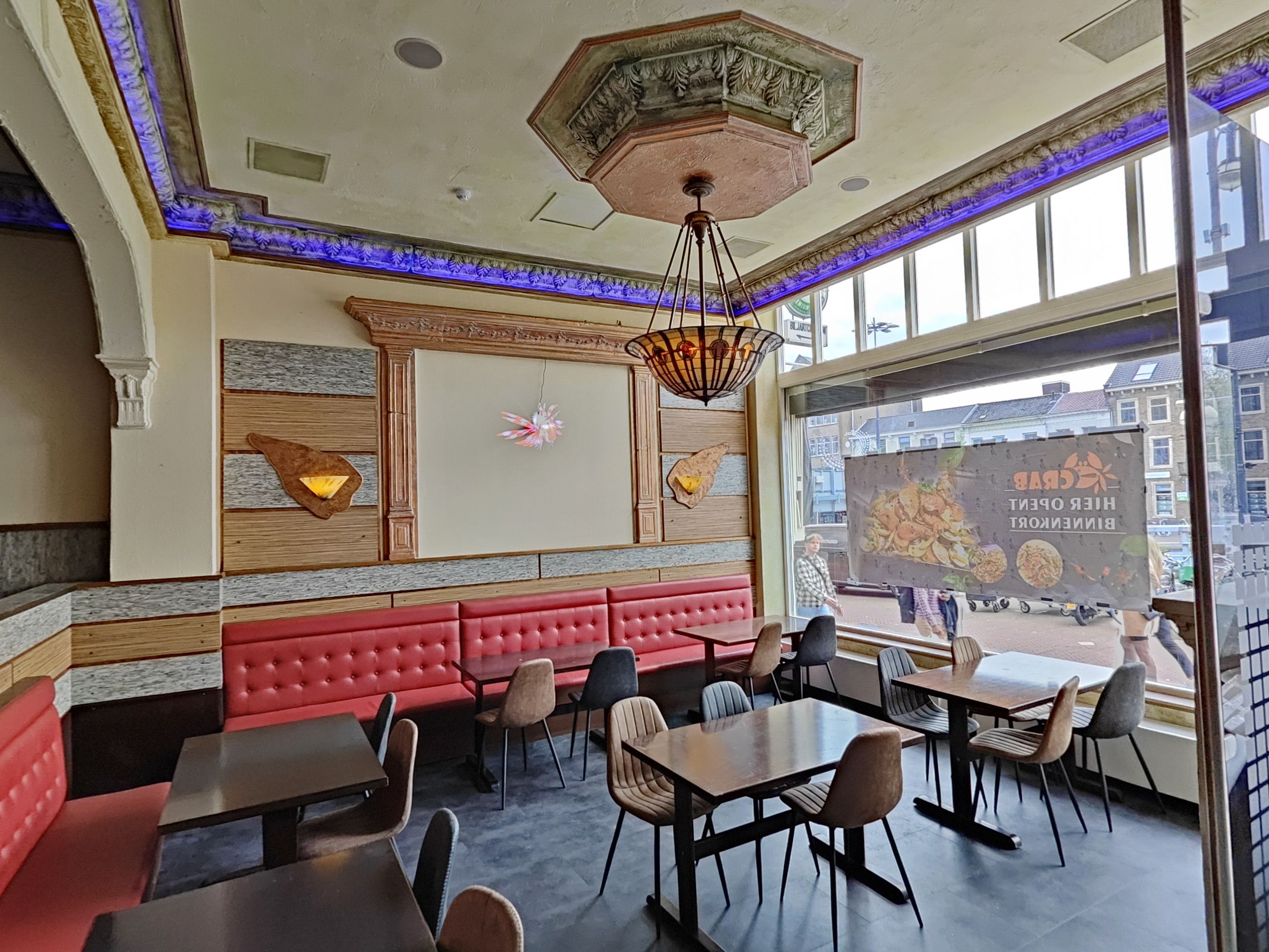 A restaurant interior with red upholstered booths, wooden panel walls, and a large window with a city view.