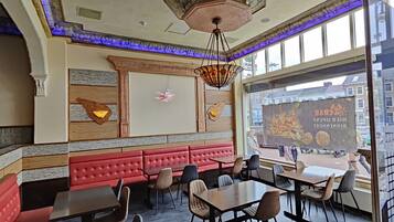 Interior de restaurante con asientos tapizados en rojo, paneles de madera en las paredes y un amplio ventanal con vista a la ciudad.