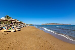 Una spiaggia con lettini e ombrelloni, cielo sereno e un'isola in lontananza.