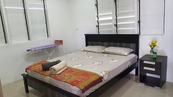 Un dormitorio ordenado con cama, mesitas de noche y un tablero para planchar.