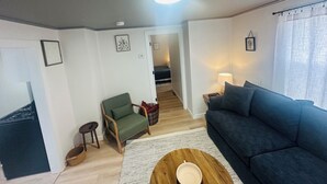 Un salon avec un fauteuil vert, un canapé bleu, une table basse en bois et une lampe sur une table d’appoint.