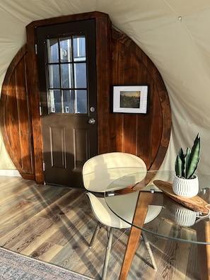 Een tent met een houten deur, een lijst met een foto, een glazen tafel, een stoel en een potplant.