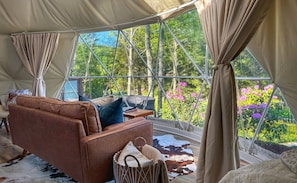 Een tent met uitzicht op een tuin, een bruine leren bank, een kleine tafel en een gevlochten mand.
