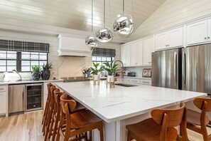 A modern kitchen with a large island, stainless steel appliances, and wooden chairs.