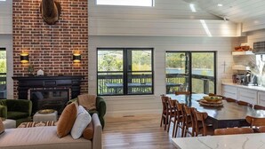 Amplia sala de estar con chimenea, mesa de comedor y cocina con ventanas grandes.