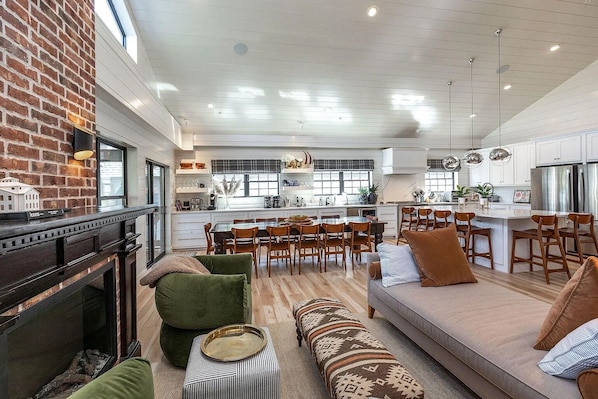 A spacious living area with a fireplace, a dining table, and a kitchen in the background.