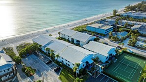 A coastal hotel with multiple buildings, a tennis court, and a beach view.