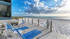 A beachside deck with blue lounge chairs and a wooden fence.