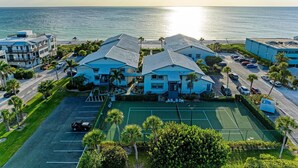A beachfront hotel with multiple buildings, a tennis court, and a parking area.