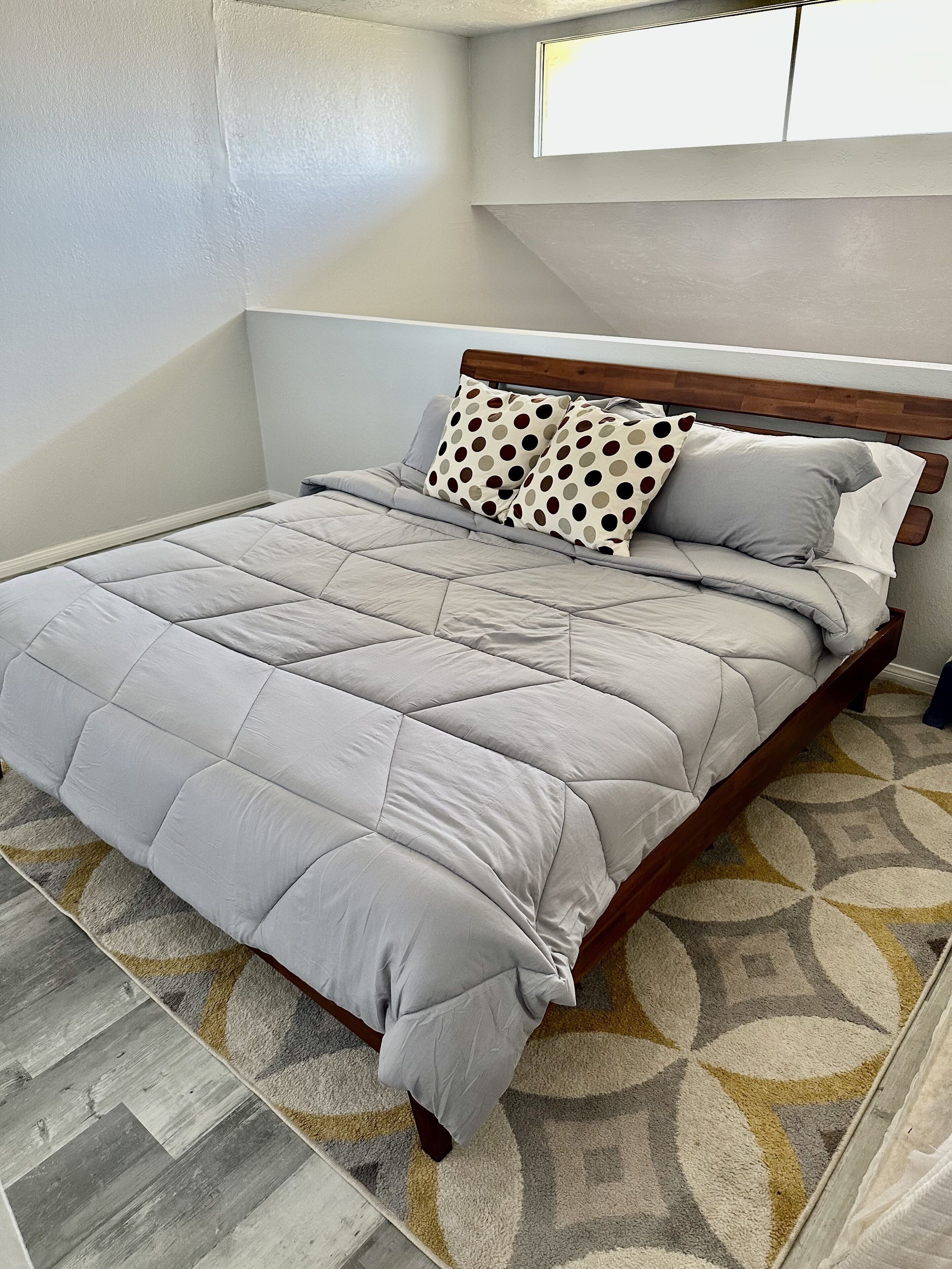 A neatly made bed with a grey quilt and two pillows, one with a polka dot pattern.