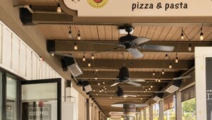 An outdoor seating area of Giuseppe's Pizza & Pasta with tables and chairs, ceiling fans, and hanging lights. - Smoke Tree Racquet Club Condo 7 min Drive to Downtown Palm Springs!  (Palm Springs)