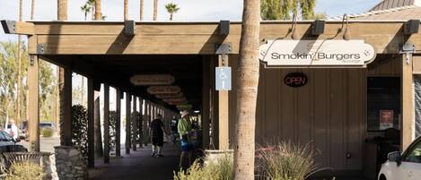 An outdoor seating area with a covered walkway, palm trees, and a sign for Smokin' Burgers & Lounge.