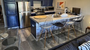 A modern kitchen with stainless steel appliances, a marble countertop, and a central island with bar stools. - Smoke Tree Racquet Club Condo 7 min Drive to Downtown Palm Springs!  (Palm Springs)