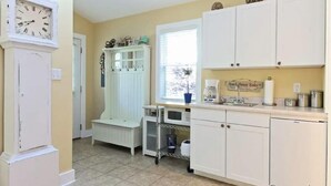 A kitchen with white cabinets, a clock, a microwave, and a coffee maker. - Charming New Buffalo Cottage (New Buffalo)