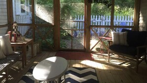A covered porch with a wooden bench, a table, and a sofa. There is a white picket fence visible through the glass doors. - Charming New Buffalo Cottage (New Buffalo)