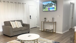 Una sala de estar moderna con un sofá gris, una mesa redonda de centro y un televisor de pantalla plana montado en la pared.