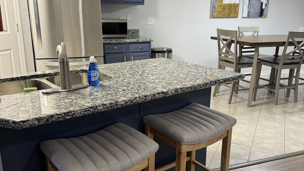 Una cocina moderna con armarios azul oscuro, un refrigerador de acero inoxidable, una encimera de granito y taburetes de madera.