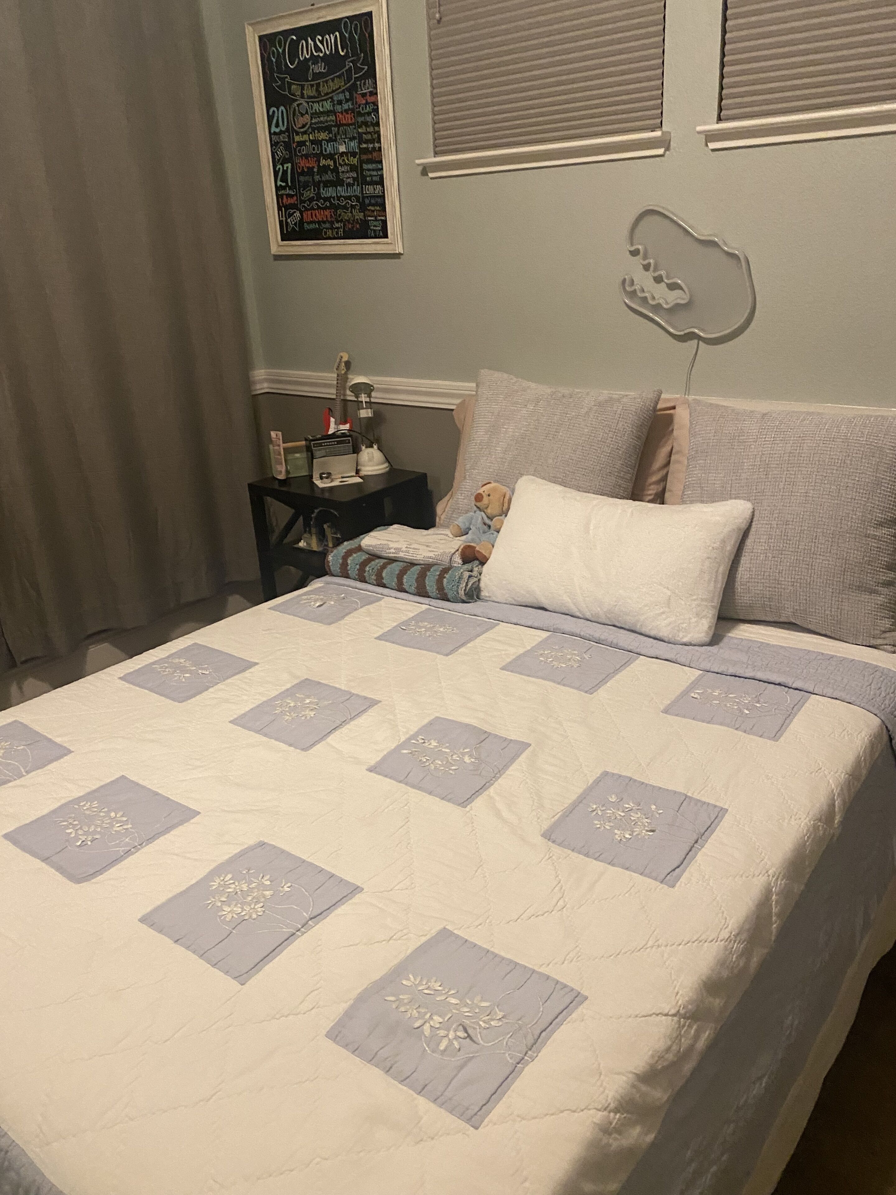 A bedroom with a bed, pillows, a nightstand, a lamp, and a wall decoration.