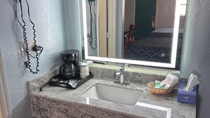A bathroom with a granite sink, a hairdryer, a coffee maker, and a trash bin. - Tanglewood Motel (Frederick)