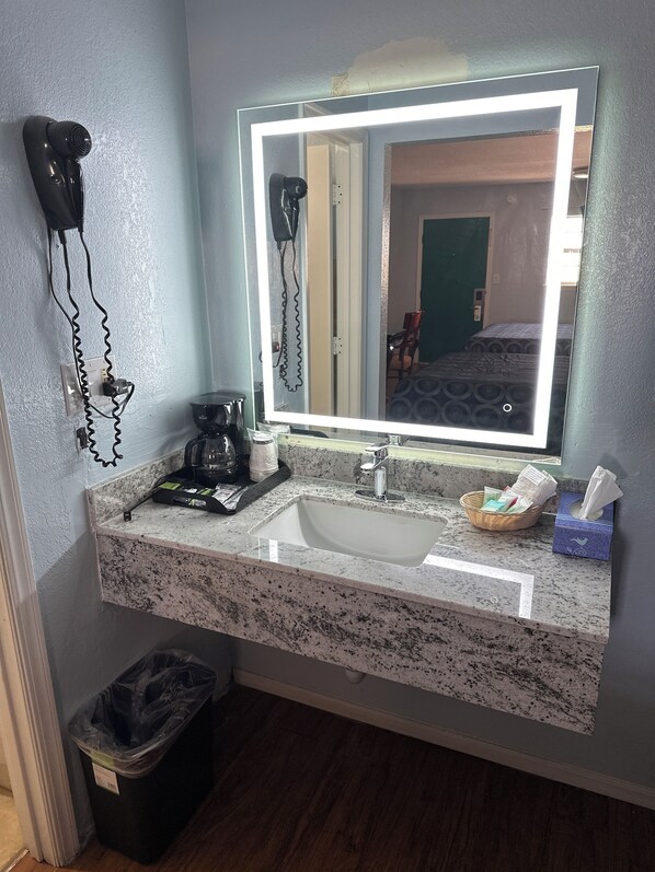 Un baño con lavamanos de granito, secador de pelo, cafetera y cubo de basura.