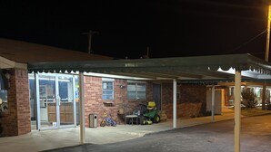 A covered parking area with a brick building in the background. - Tanglewood Motel (Frederick)